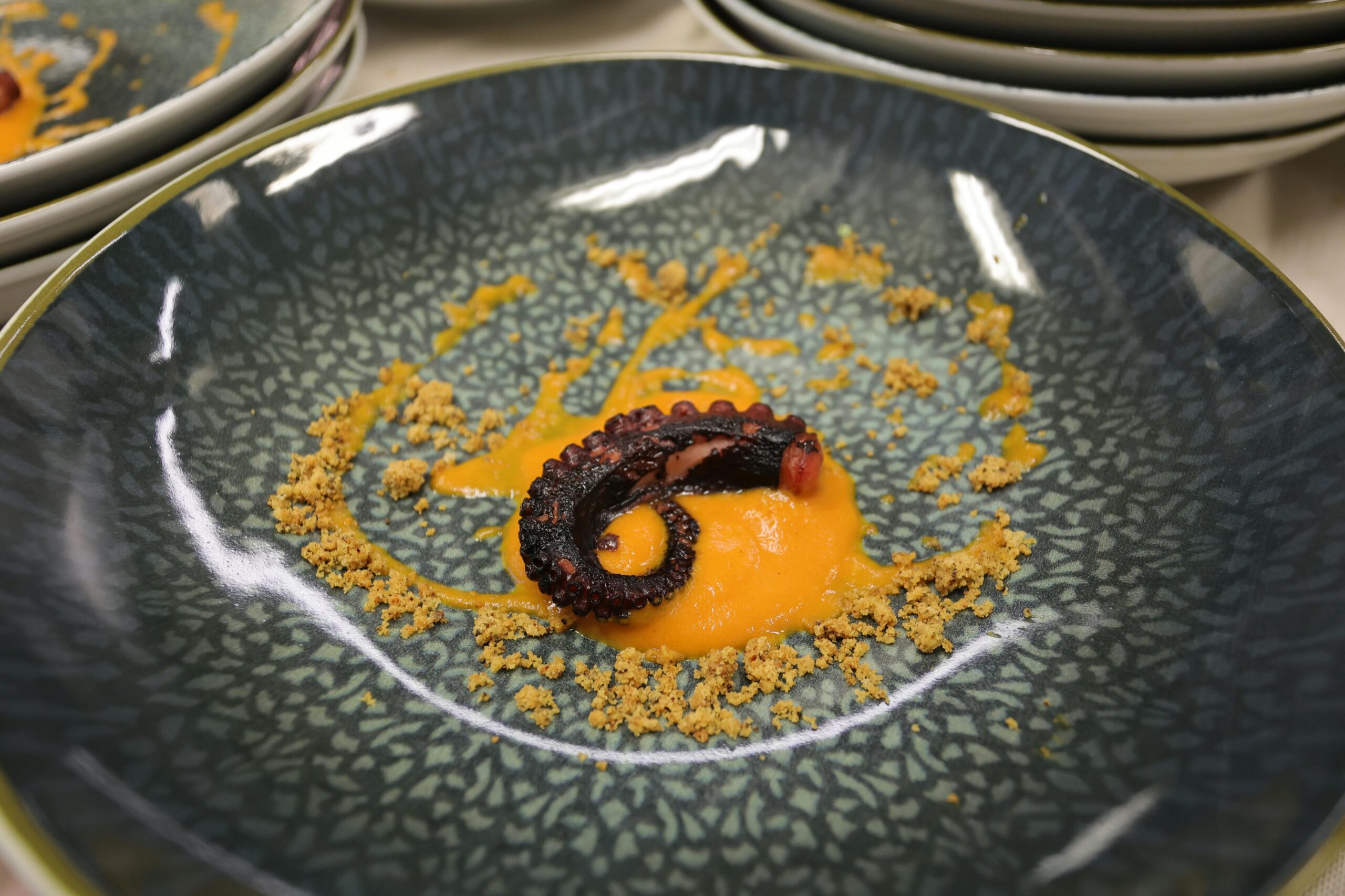 Elegant octopus tentacle on a ceramic plate with orange sauce and breadcrumbs, showcasing gourmet cuisine.